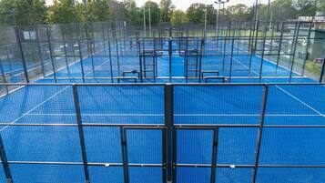 En tennisplan med nät, omgiven av ett staket, och träd i bakgrunden.