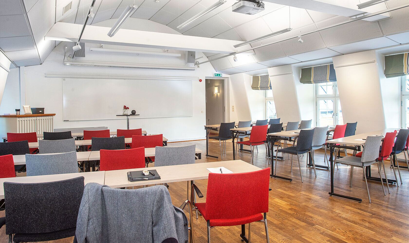 Une salle de classe avec des rangées de bureaux et de chaises, un tableau blanc et un projecteur.