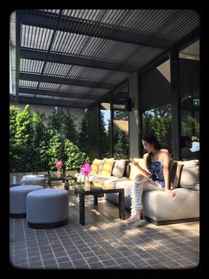 An outdoor seating area with a sofa and ottomans, a coffee table, and a flower vase. - Happy 3 (Bangkok)