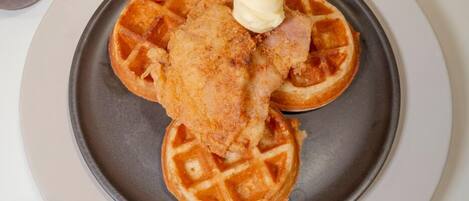 Un plato con dos waffles y un trozo de pollo frito sobre un fondo oscuro.