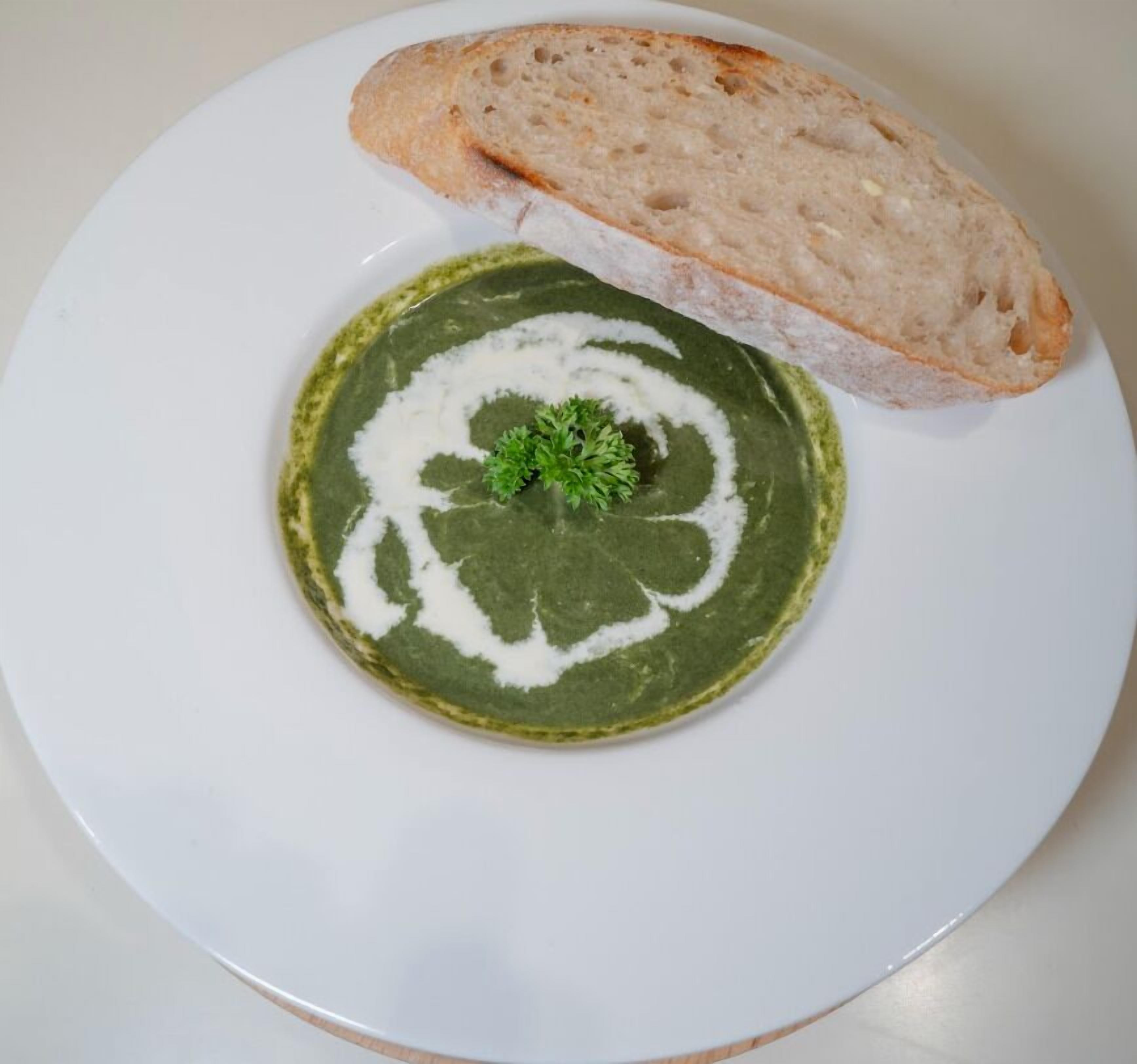 A plate with a green soup and a slice of bread.