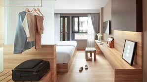A modern hotel room with a bed, a wooden bench, a suitcase, and a clothing rack with hangers. - Happy 3 (Bangkok)