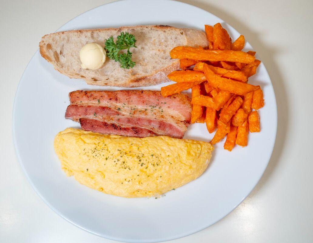 A plate with toast, bacon, sweet potato fries, and scrambled eggs.