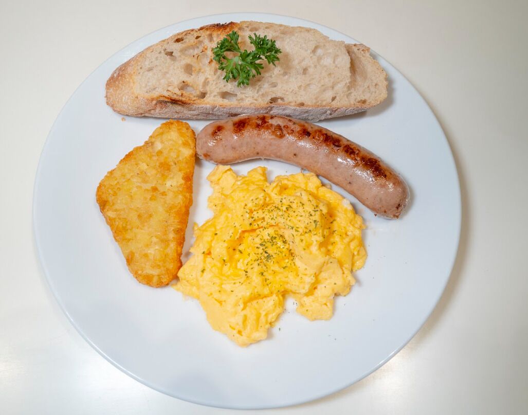 Une assiette avec des œufs brouillés, une saucisse et une tranche de pain.
