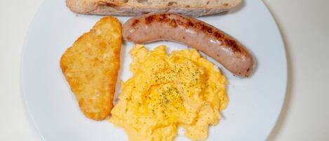 Une assiette avec des œufs brouillés, une saucisse et une tranche de pain.