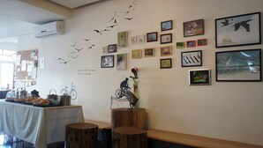 Una habitación con una pared decorada con cuadros enmarcados y un adhesivo de aves volando. Hay una mesa con comida y un banco de madera.