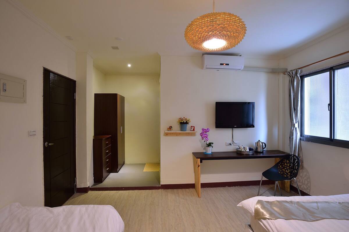 A hotel room with a bed, a desk with a chair, a television, and a window with curtains.