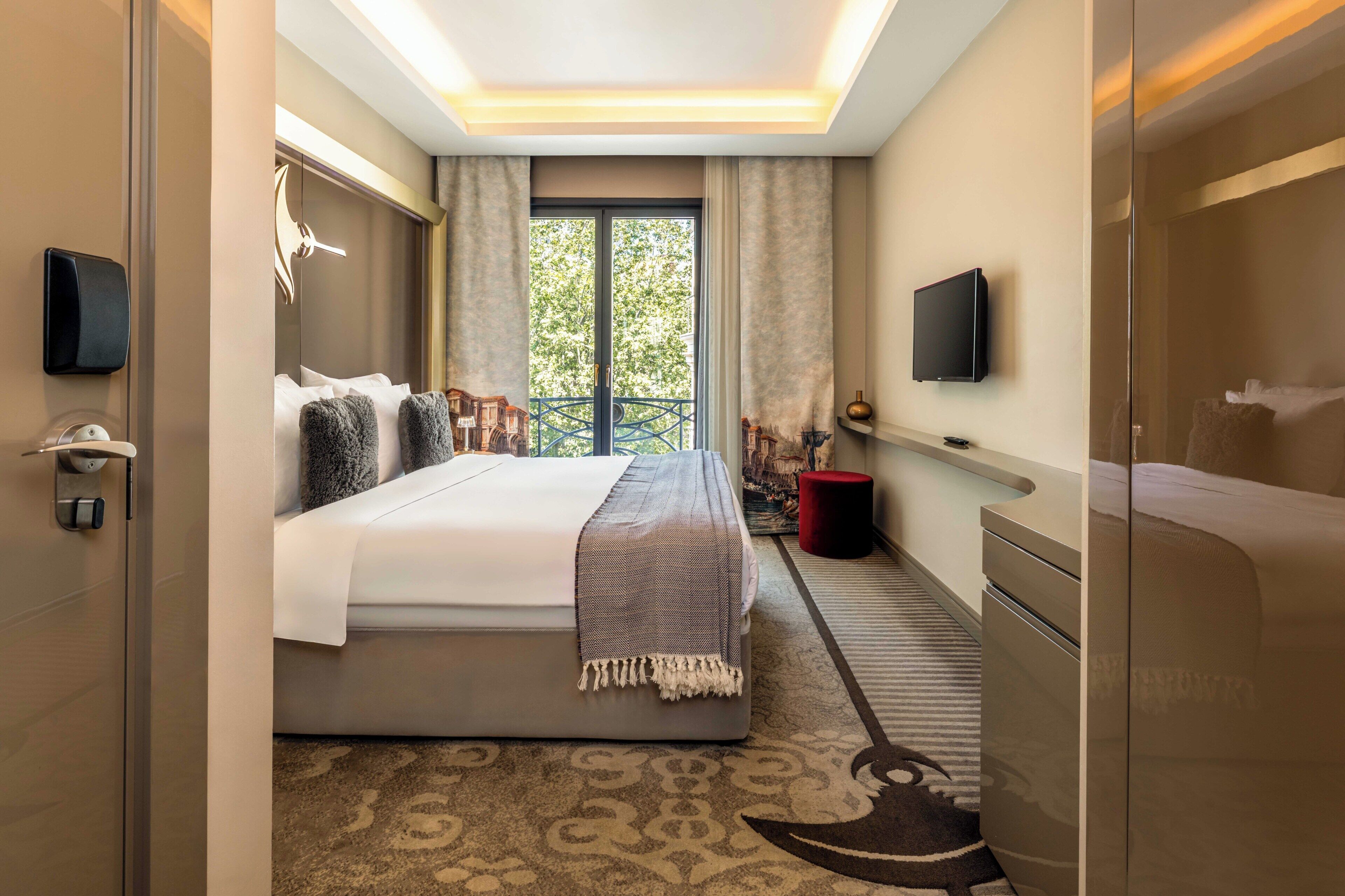 A hotel room with a bed, a TV, a balcony, and a desk.