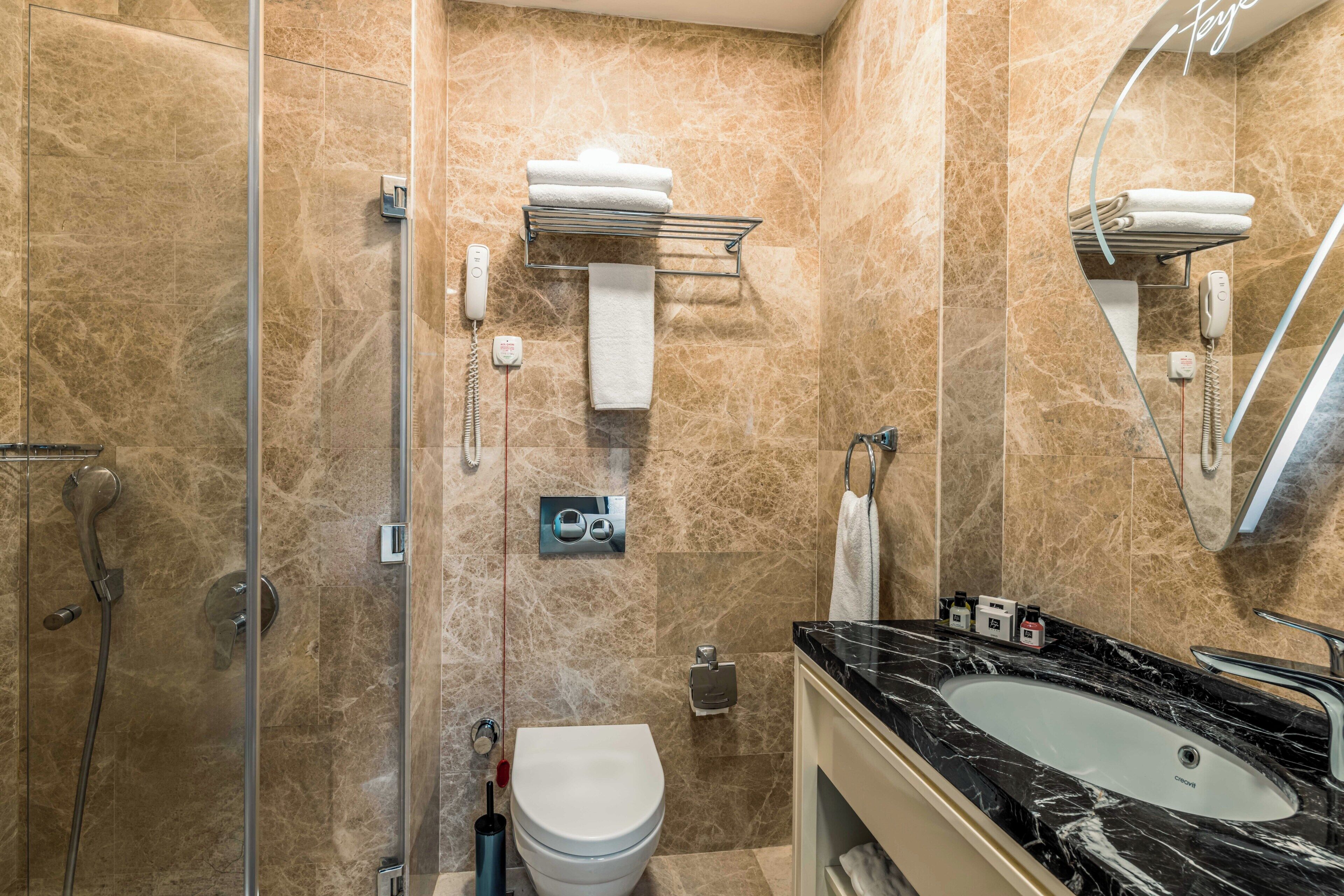 A bathroom with a glass shower enclosure, a white toilet, a black marble sink, and a towel rack.