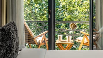 Uma varanda com mesa de madeira, duas cadeiras e vista para vegetação exuberante.