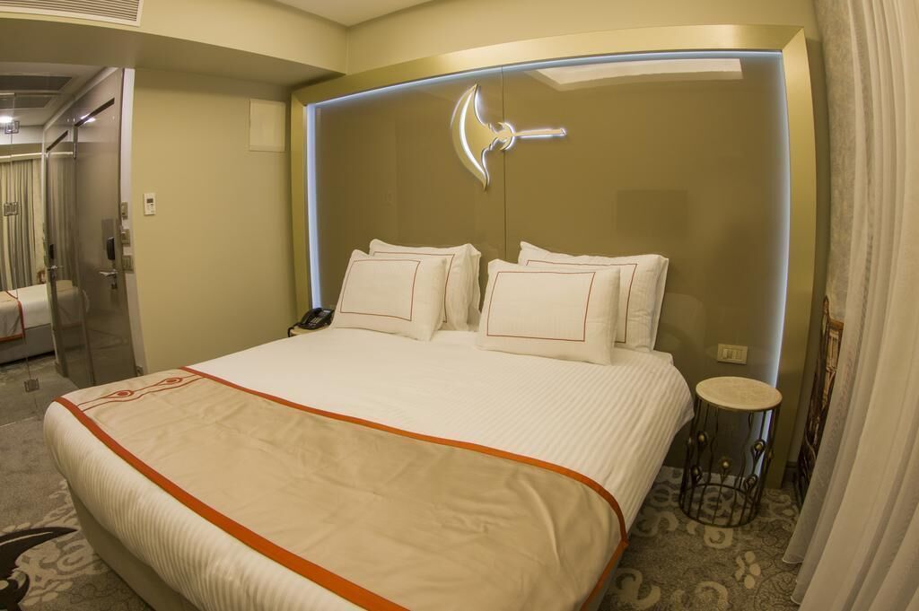 A hotel room with a large bed, a bedside table, a mirror, and a door leading to a bathroom.