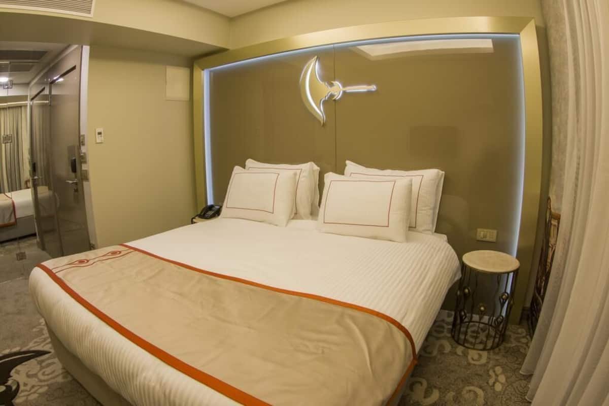A hotel room with a large bed, a bedside table, a mirror, and a door leading to a bathroom.