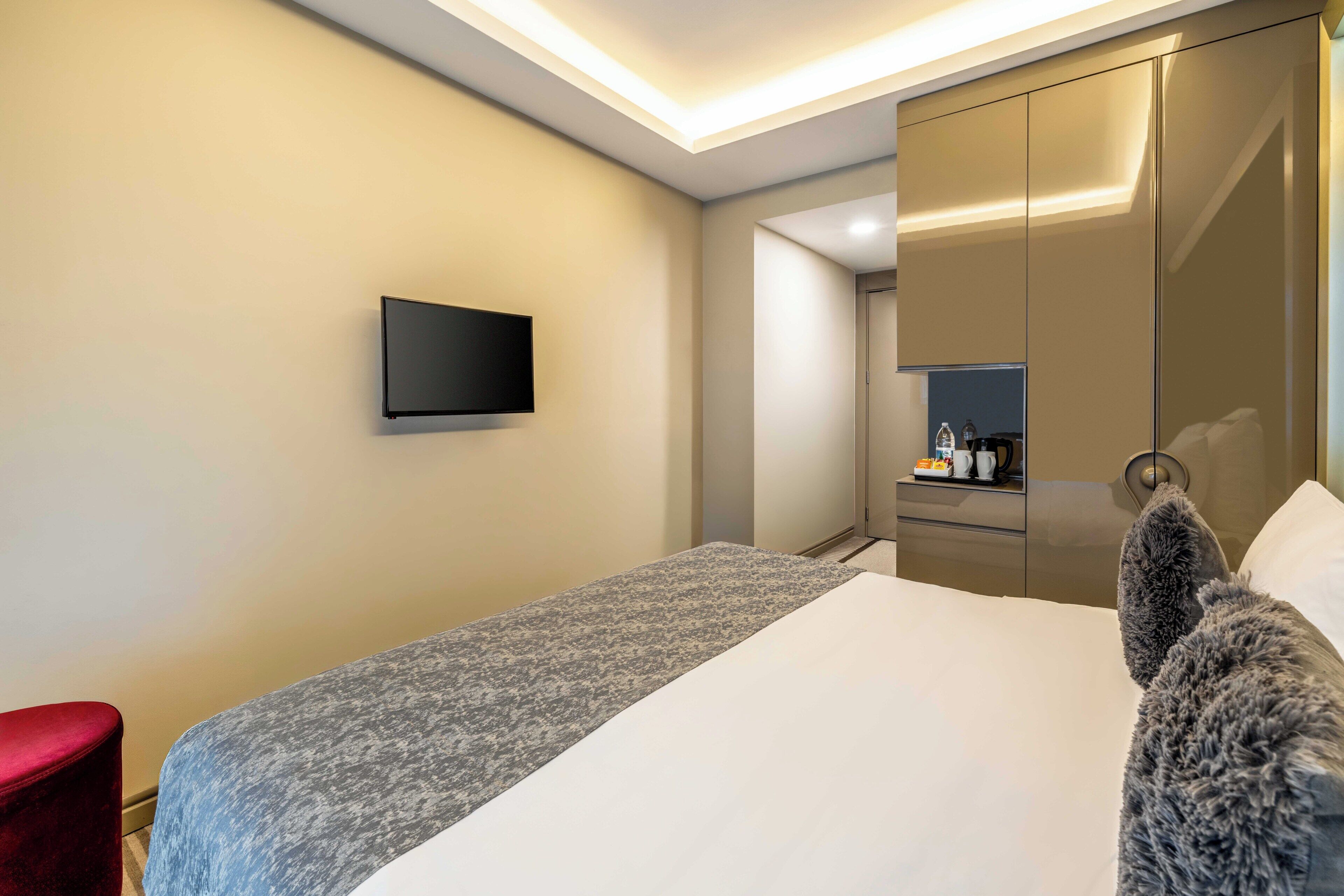 Een hotelkamer met een bed, een flatscreen televisie, een rode stoel, een kledingkast en een spiegel.