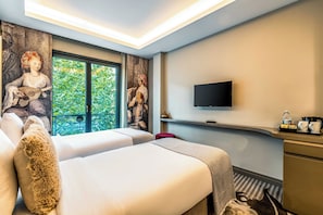 A hotel room with two beds, a TV, a window with a view of greenery, and a painting on the wall. - Peyk Hotel Sultanahmet (Istanbul)
