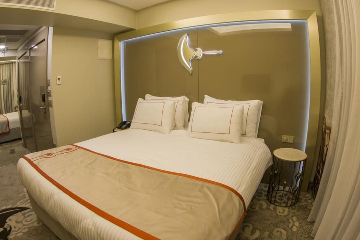 Habitación de hotel con una cama grande, una mesita de noche, un espejo y una puerta que da a un baño.