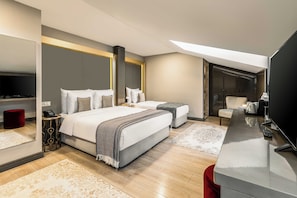 A modern hotel room with a large bed, a smaller bed, a desk, a TV, and a red ottoman. - Peyk Hotel Sultanahmet (Istanbul)