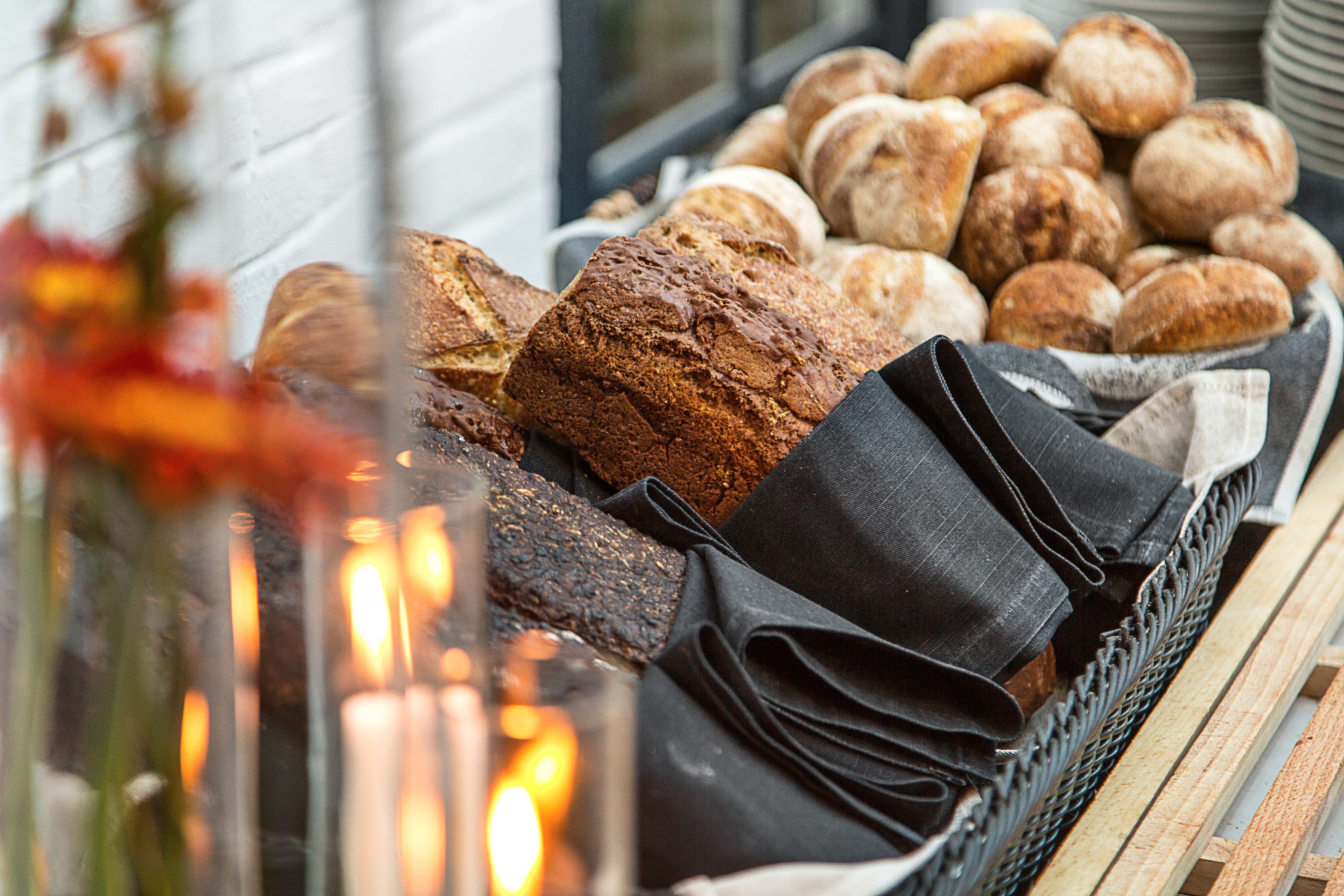 Une variété de pains et de pâtisseries sont présentés dans un panier, avec une bougie et un tissu noir à proximité.
