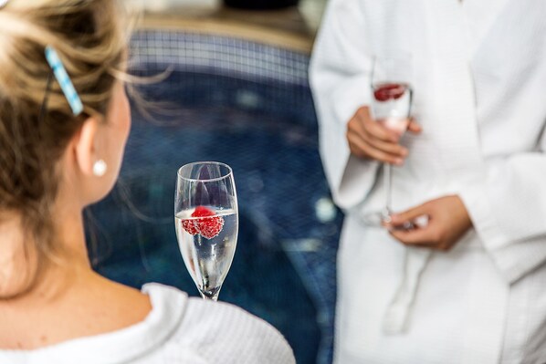 A person holding a champagne glass with a red fruit garnish, standing near a pool. - Hotell Gässlingen (Skanör)