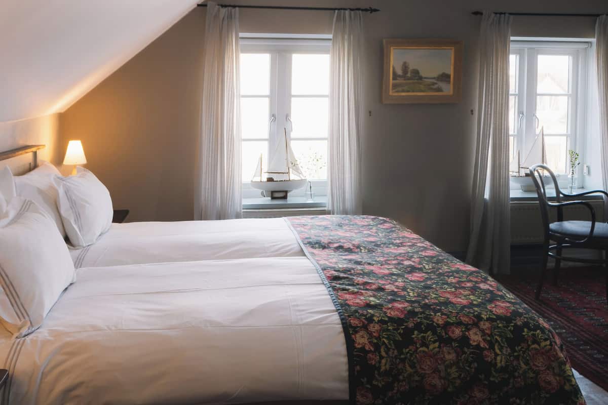 Quarto com uma cama grande, duas mesas de cabeceira, uma cadeira e uma janela com cortinas.