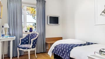 Une chambre à coucher avec un lit, un bureau, une chaise, une télévision et une fenêtre avec des rideaux.