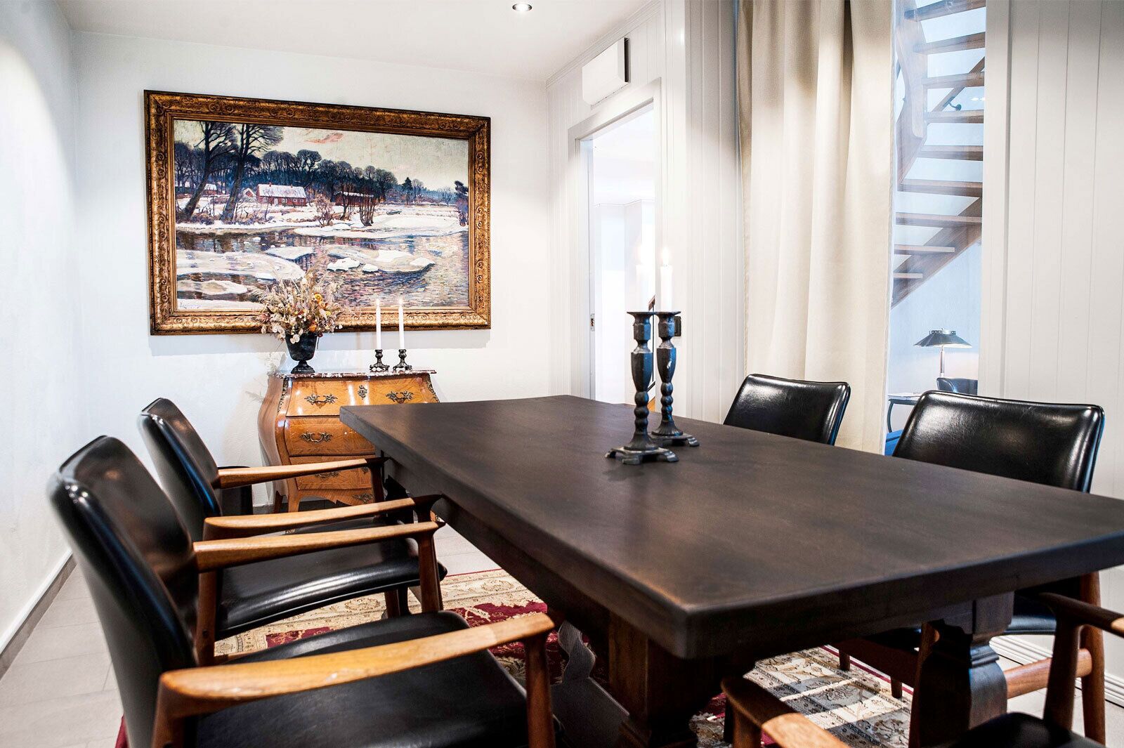 Un comedor con una mesa de madera oscura, seis sillas, un cuadro y un jarrón con flores.