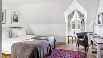 Une chambre avec deux lits, un bureau, une chaise, une fenêtre avec des rideaux et un tapis à motifs.