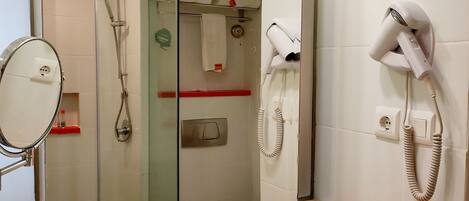 A hotel bathroom with a sink, mirror, hairdryer, and shower.