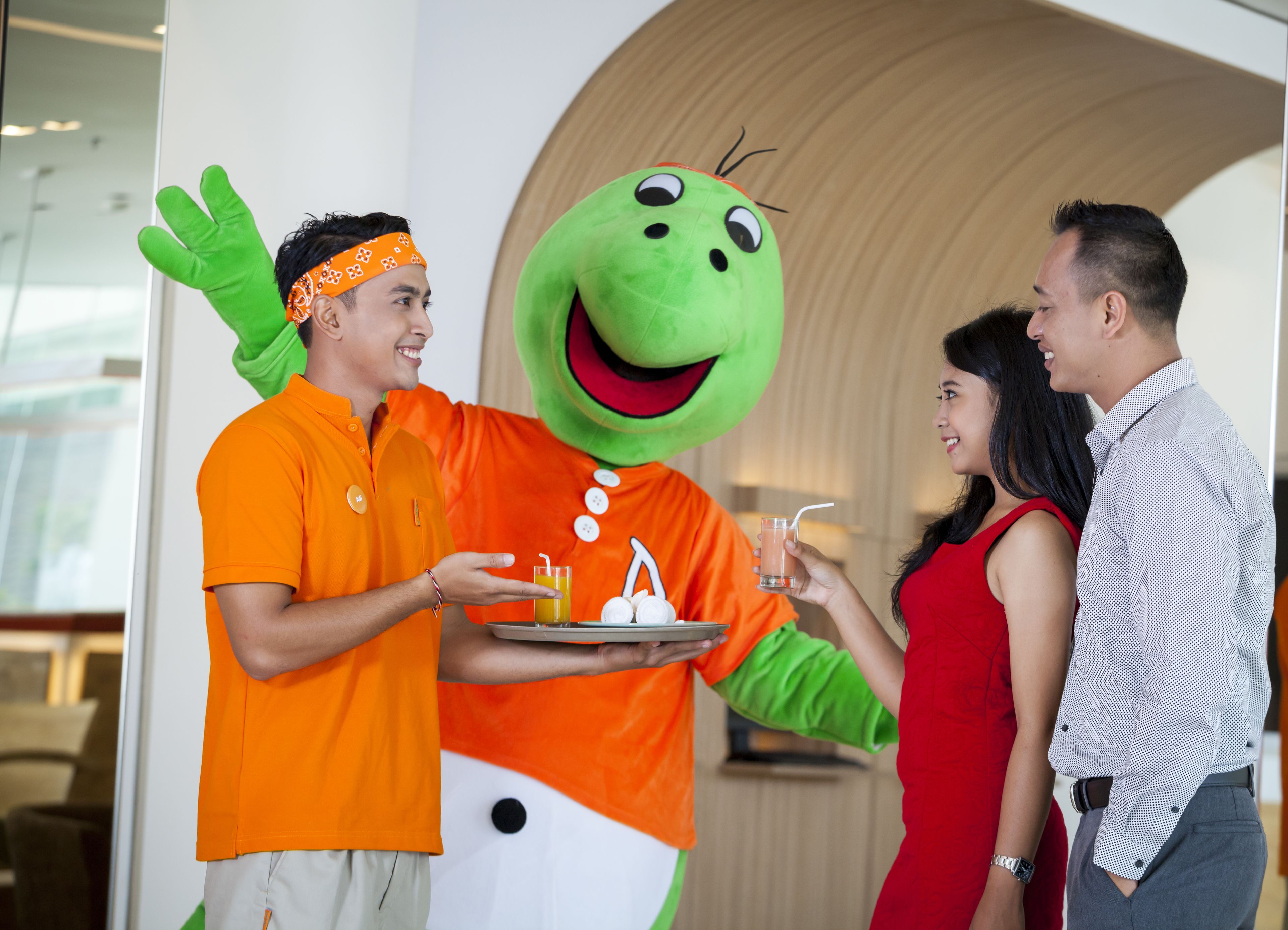 A person in a green mascot costume serving drinks to guests in a modern indoor setting.