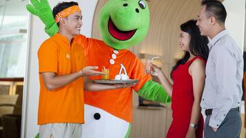 A person in a green mascot costume serving drinks to guests in a modern indoor setting.