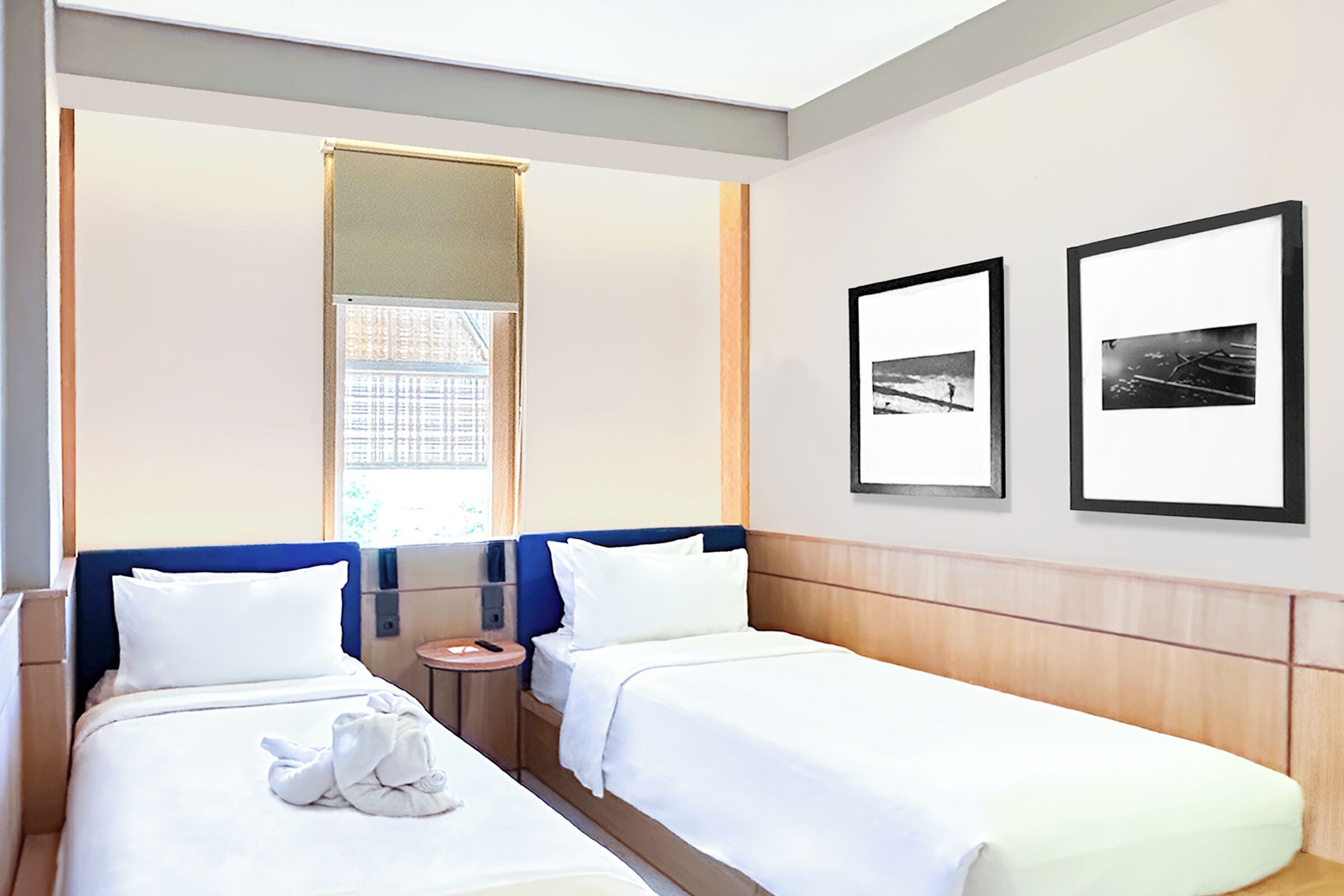 Una habitación de hotel con dos camas, una mesita redonda pequeña y dos cuadros en la pared.