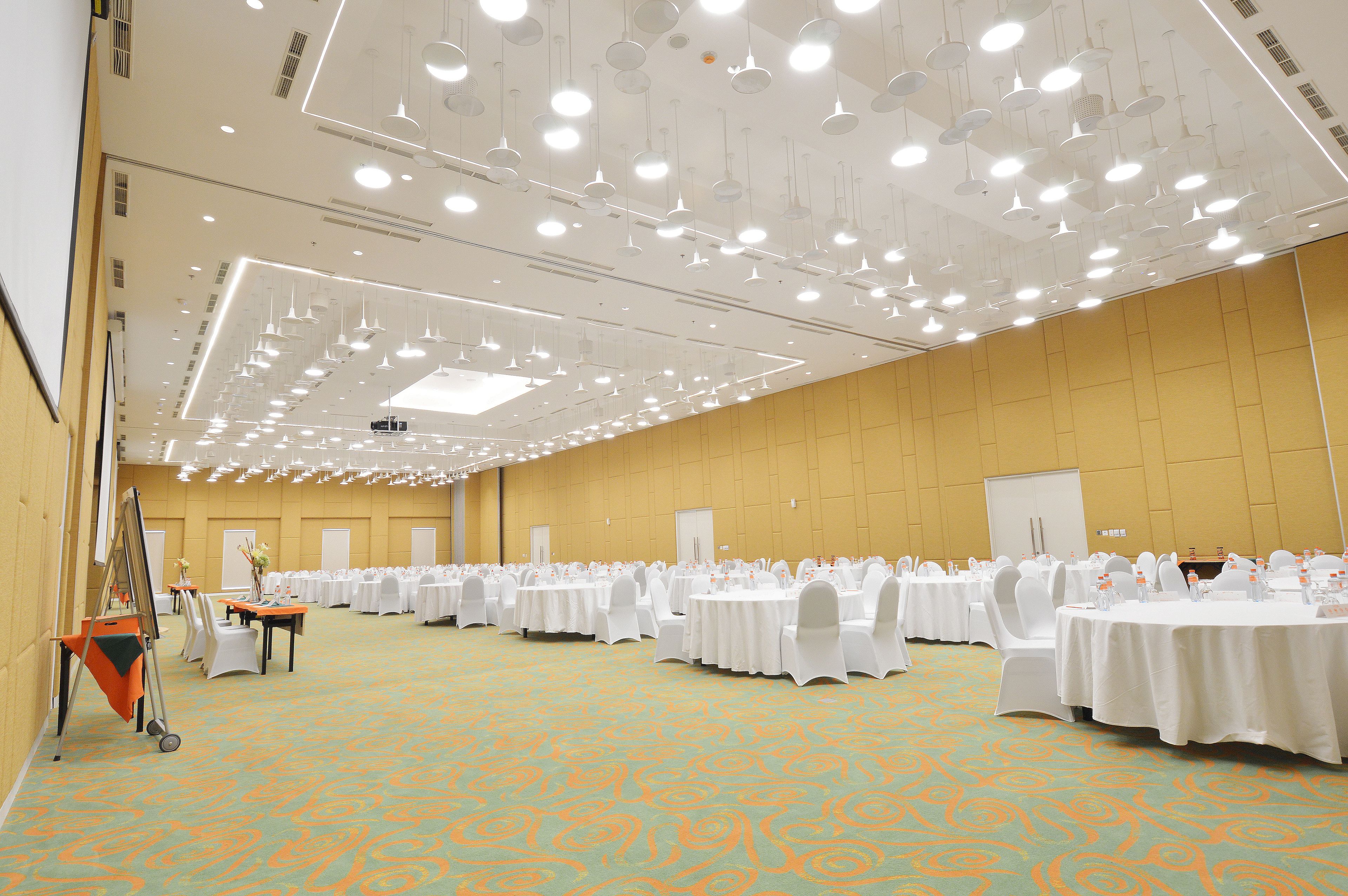 A large conference room with rows of round tables, white chairs, and a carpeted floor.