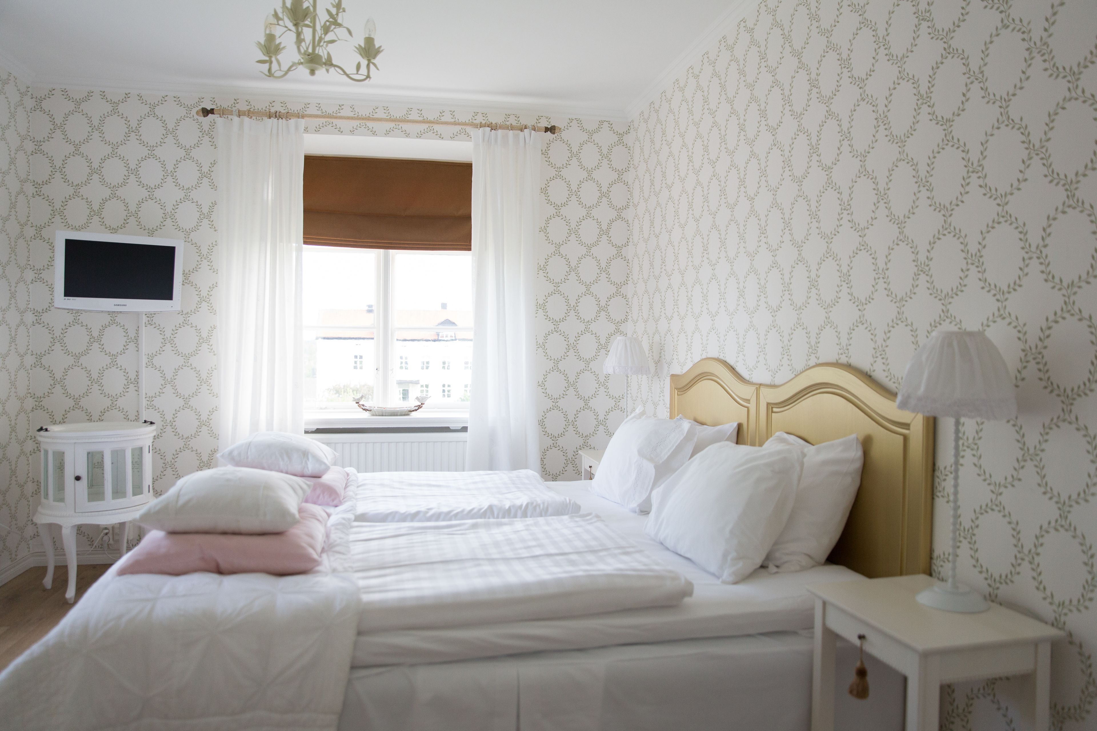 Habitación de hotel con dos camas, televisión, ventana con cortinas y una mesita.