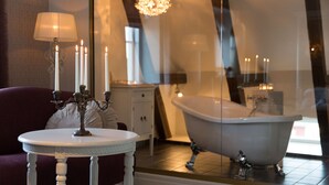Een badkamer met een wit bad, een ronde witte tafel met kaarsen, en een spiegel die de ruimte weerspiegelt.