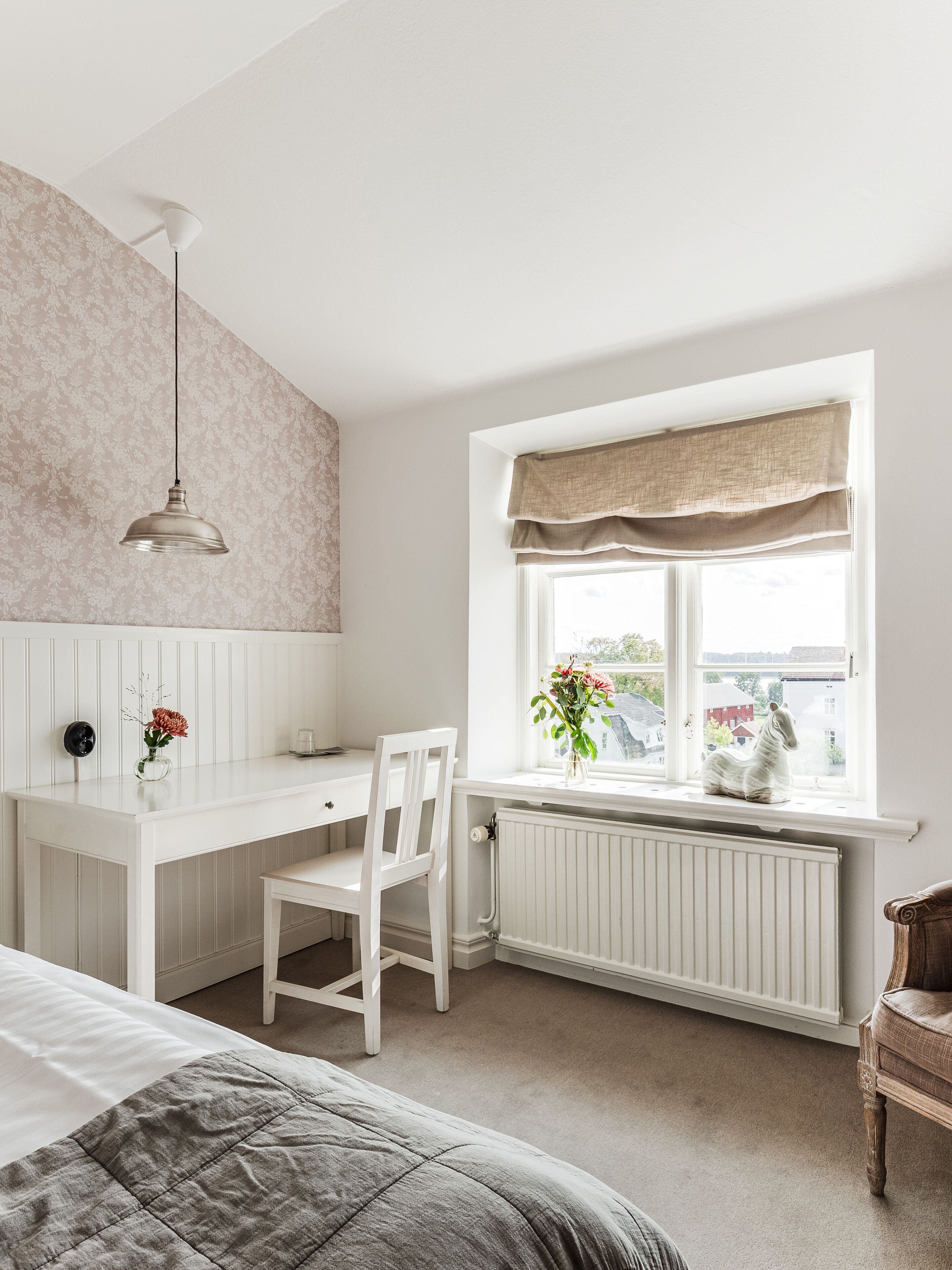 Ein Schlafzimmer mit Bett, Schreibtisch und Stuhl. Ein Fenster bietet einen Ausblick nach draußen.