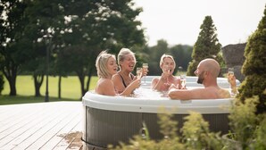 Een groep mensen in een bubbelbad buiten, omringd door groen.