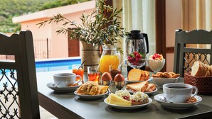 A breakfast table with various food items, a coffee pot, and a view of a pool and greenery. - Petronikolis Traditional House (Archanes-Asterousia)