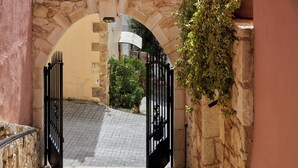 An arched stone doorway with a metal gate, leading to a cobblestone path. - Petronikolis Traditional House (Archanes-Asterousia)