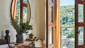 A room with a large window, a mirror, a potted plant, and a small table with decorative items. - Petronikolis Traditional House (Archanes-Asterousia)
