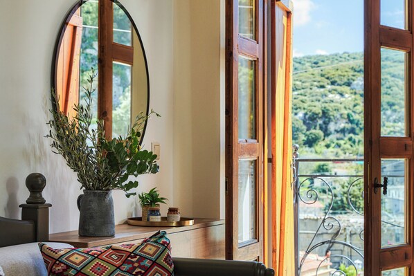 A room with a large window, a mirror, a potted plant, and a small table with decorative items.