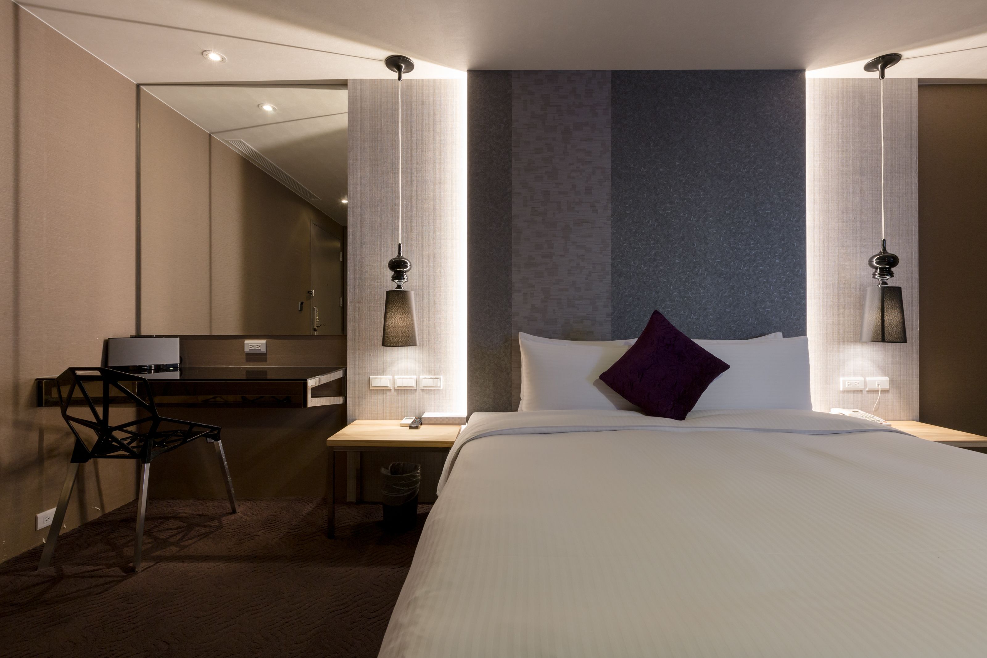 A modern hotel room with a large bed, a desk, and a chair.