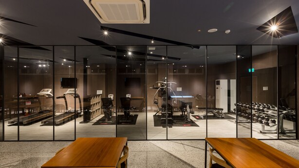 A gym with exercise equipment, a wooden table, and a large mirror wall. - Green Hotel (Magong)