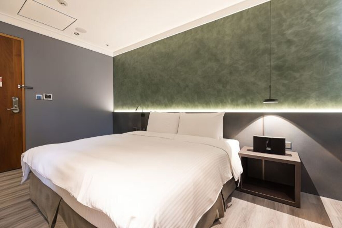 Habitación de hotel moderna con una cama grande, una mesita de noche con lámpara y una pared verde de acento.