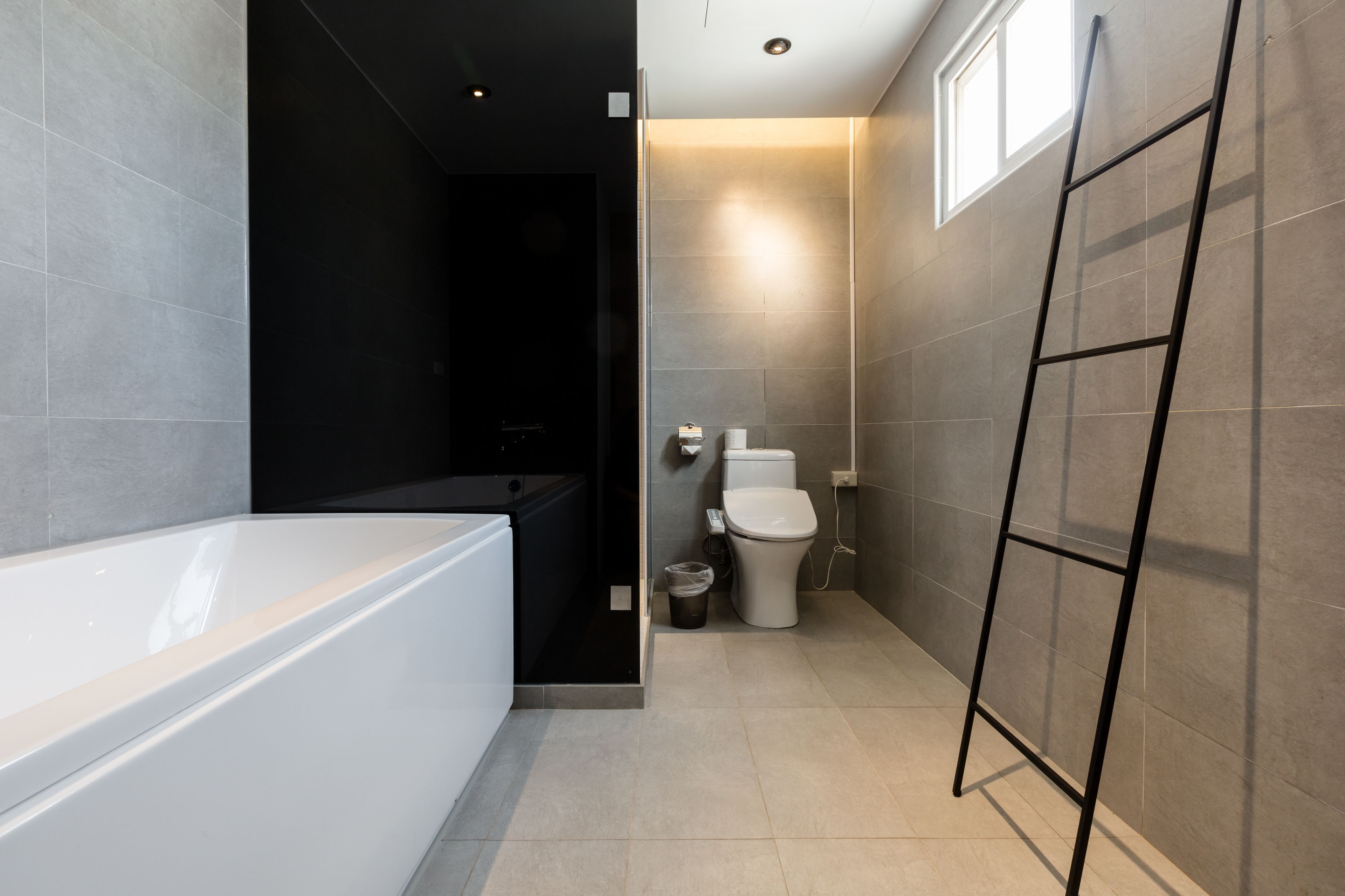 A modern bathroom with a bathtub, toilet, and a small trash bin.