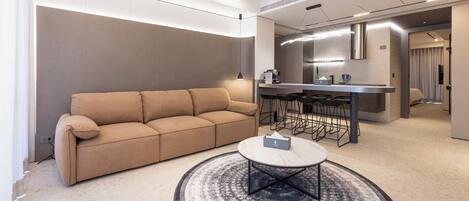 Una sala de estar moderna con un sofá beige, una mesa de centro redonda y una zona de cocina con taburetes de bar.