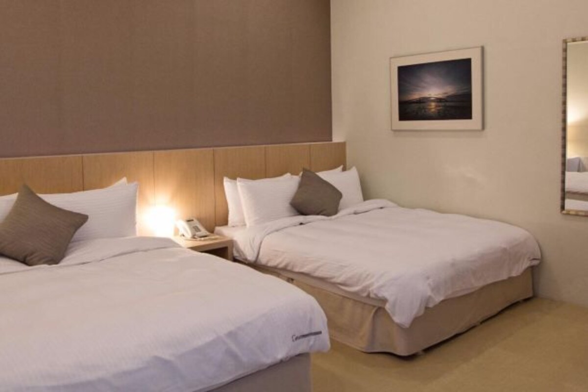 Habitación de hotel con dos camas, una mesita de noche con teléfono y un cuadro enmarcado en la pared.