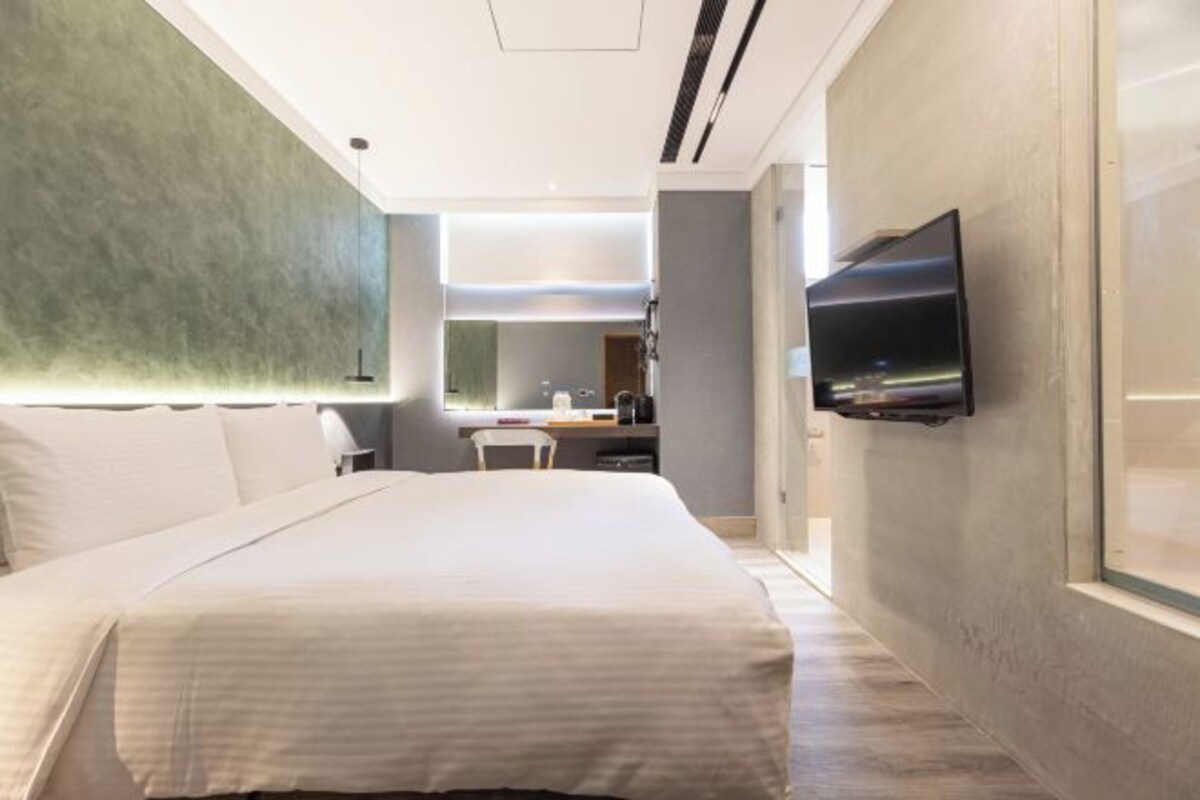 Una habitación de hotel moderna con una cama grande, un televisor de pantalla plana montado en la pared, un escritorio con una silla y vistas al interior de la habitación.