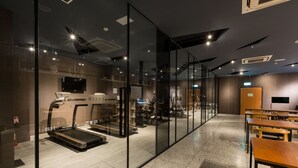 A modern fitness center with a treadmill, exercise equipment, and a glass wall separating the area. - Green Hotel (Magong)