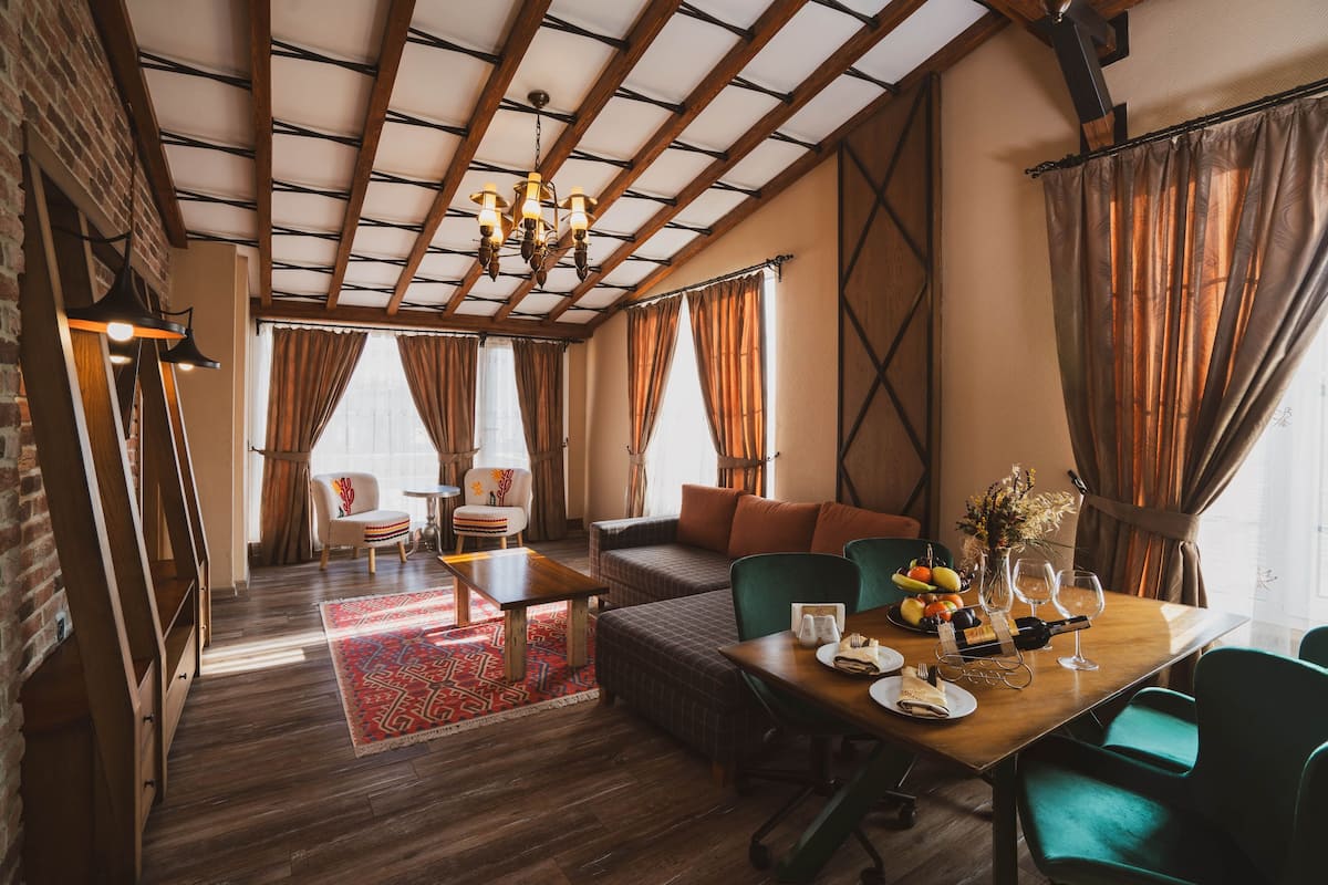 A spacious room with a wooden ceiling, a dining table set with plates, glasses, and a bottle, and a sofa with cushions.