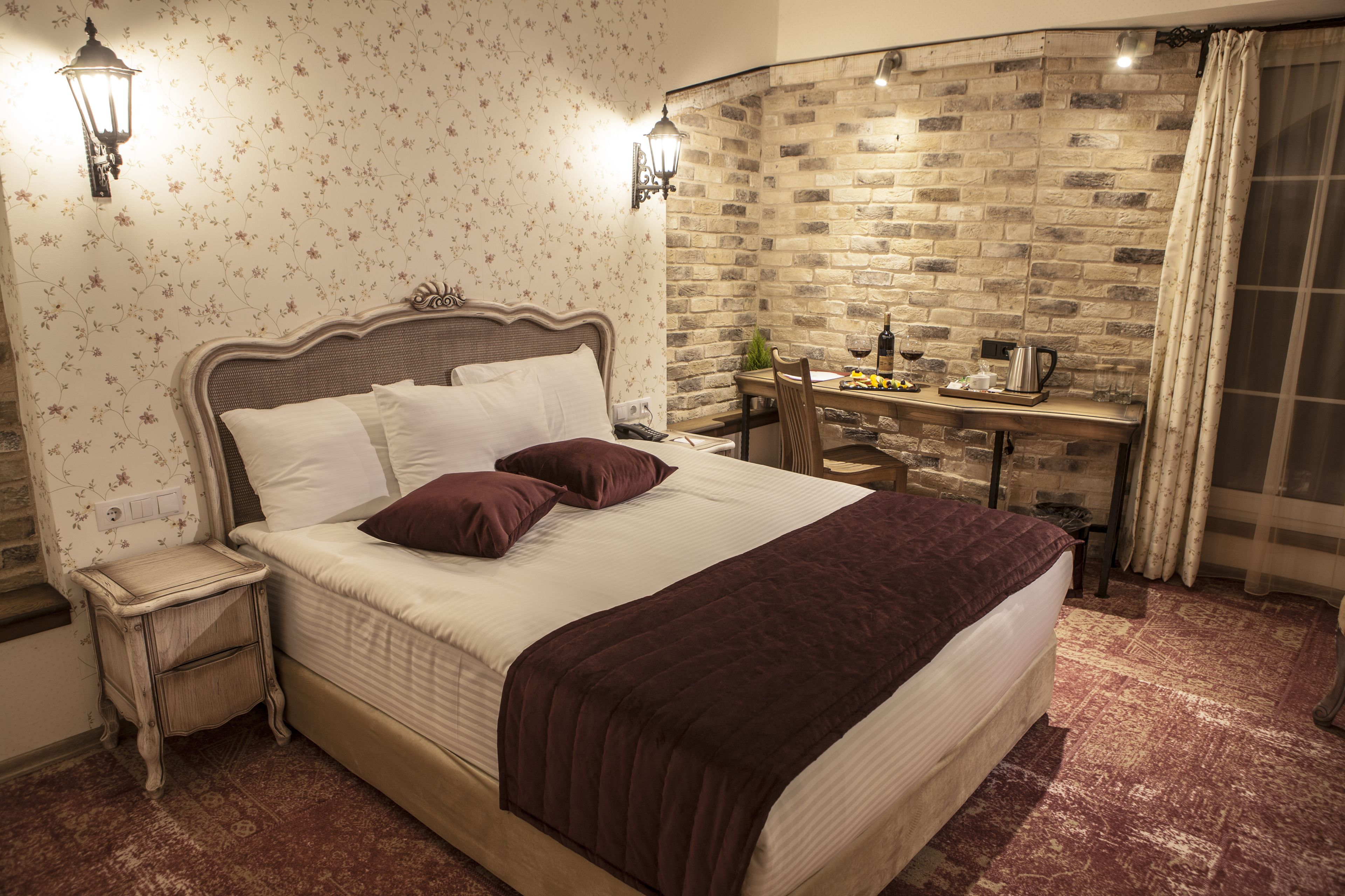 Een hotelkamer met een groot bed, een nachtkastje, een kleine tafel met lamp, en een bakstenen muur.
