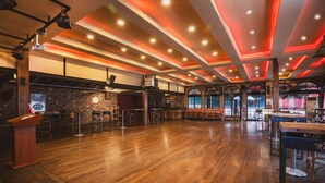 A spacious indoor area with wooden flooring, a bar area with stools, and a stage with a podium. - Raymar Hotels Ankara (Ankara)